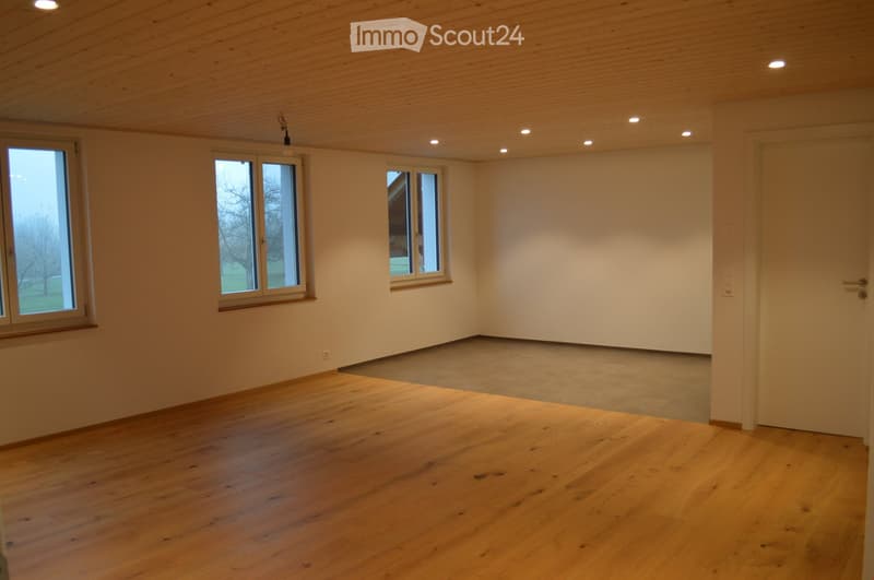 Empty room with wooden flooring, white walls, and multiple windows, including a sliding door, with recessed ceiling lighting.