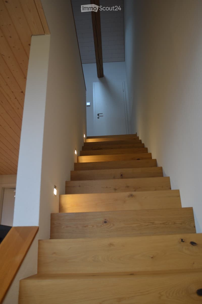 Wooden staircase with modern design, illuminated by wall-mounted lights, leading to a closed door at the end.