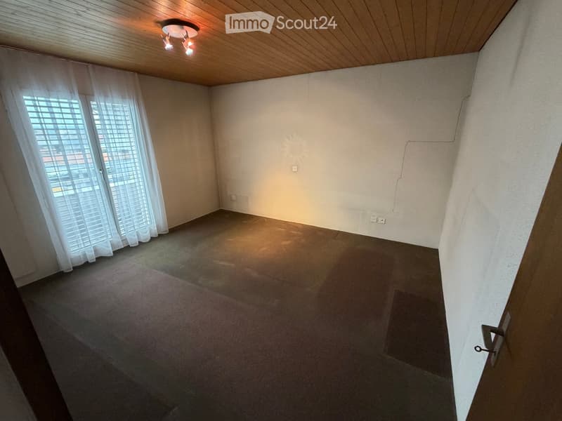 Empty room with carpeted floor, white walls, large window with blinds, and a wooden ceiling with a light fixture.
