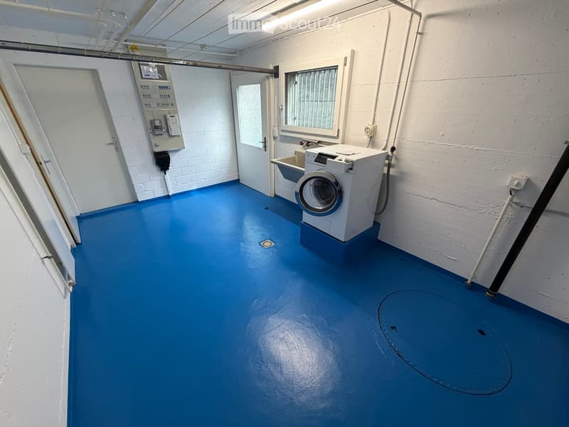 A small utility room with a blue floor, white brick walls, a washing machine, and a sink.