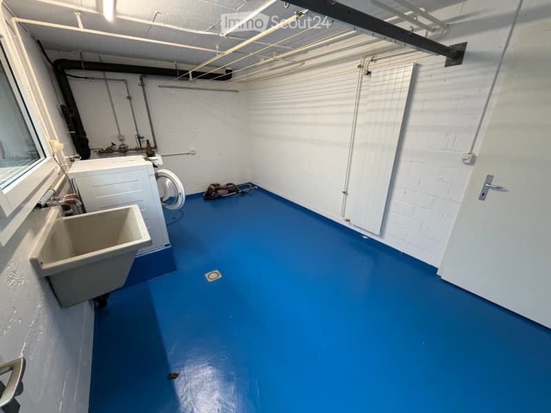Bathroom with blue flooring, white walls, a sink, and a washing machine. Exposed pipes and a window are visible.