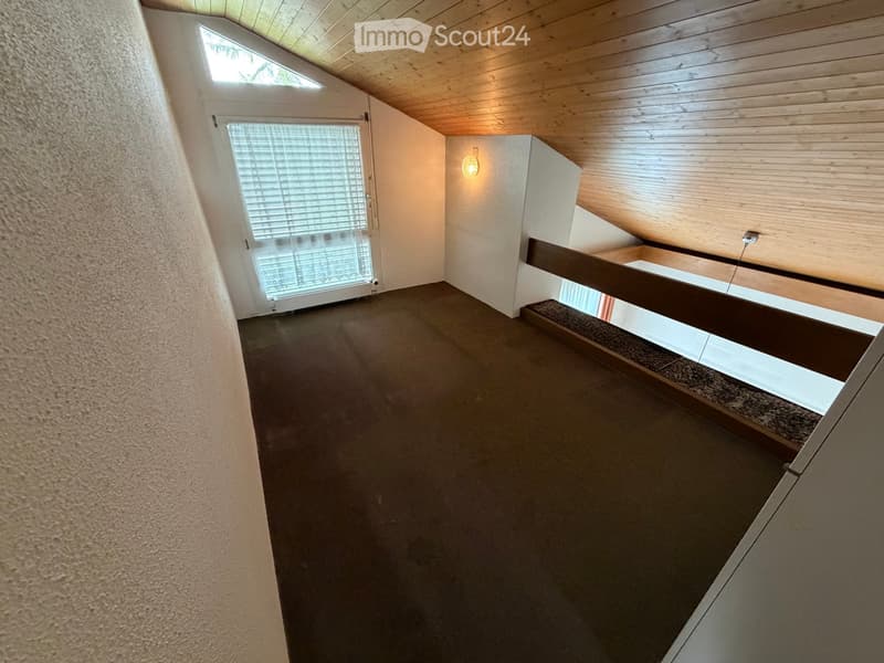 Empty hallway with wooden ceiling, carpeted floor, and a small window at the end.