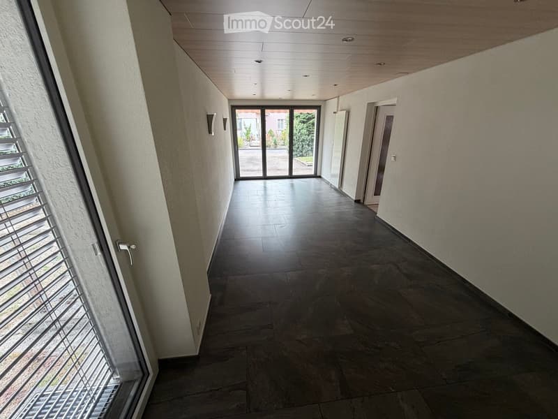 Empty hallway with tiled floor, white walls, and large sliding glass doors leading outside.