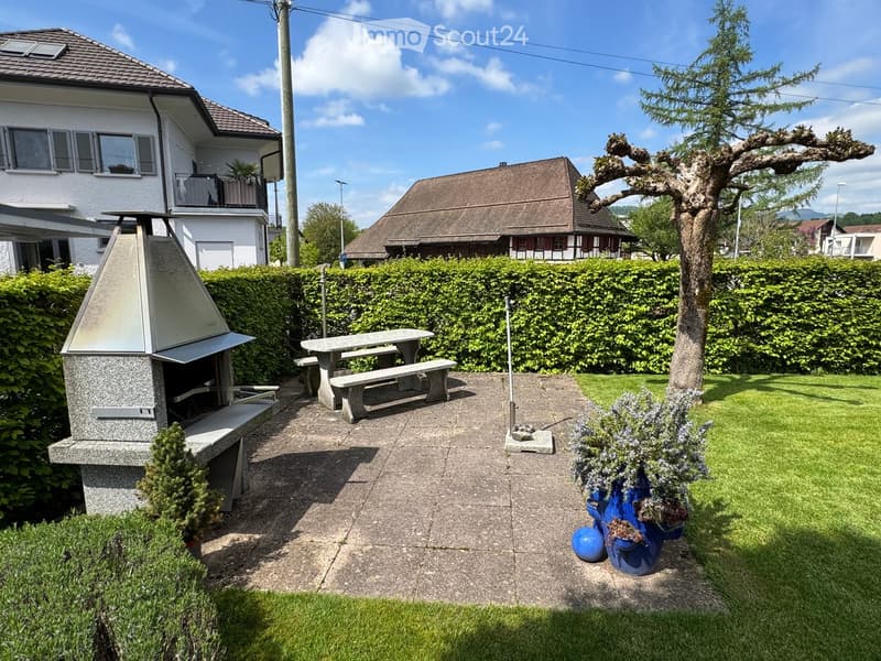 Well-maintained garden with a stone barbecue, picnic table, benches, and decorative blue vases with plants.
