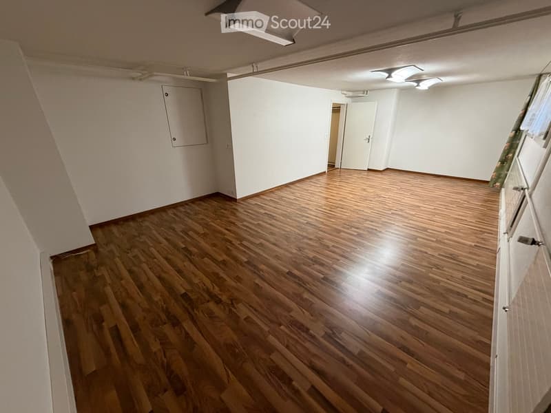 Empty room with wooden flooring and white walls, featuring a door and a small cabinet.