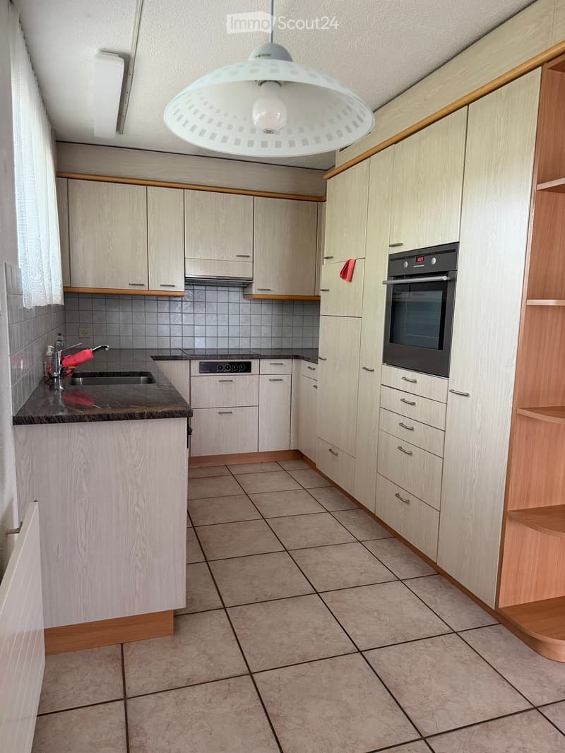 Modern kitchen with light wood cabinets, granite countertop, tiled floor, and built-in oven.