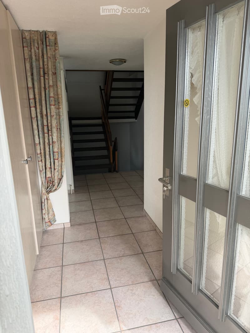 Empty hallway with tiled floor, wooden door on the left, and staircase leading upwards in the background.