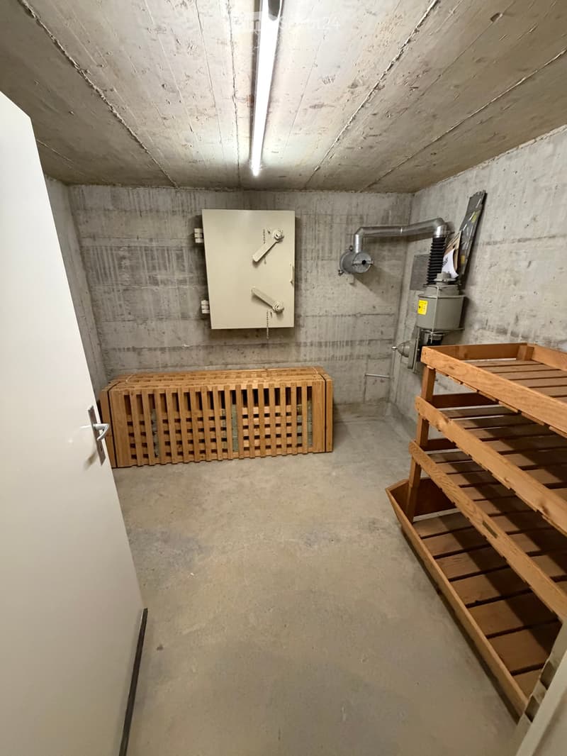 Empty concrete room with wooden shelving, a wooden radiator cover, and a control panel on the wall.