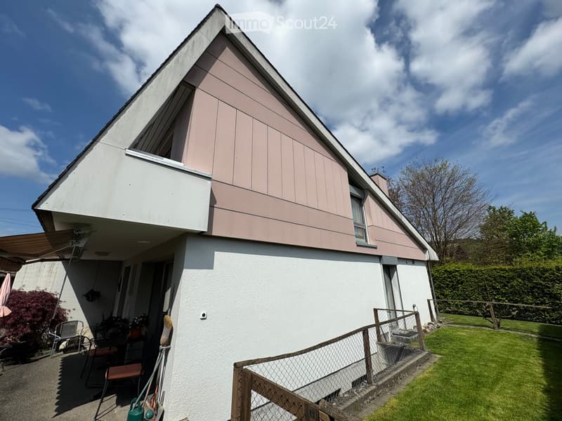 Two-story house with white and pink exterior, raised ground floor, small garden, and outdoor seating area.