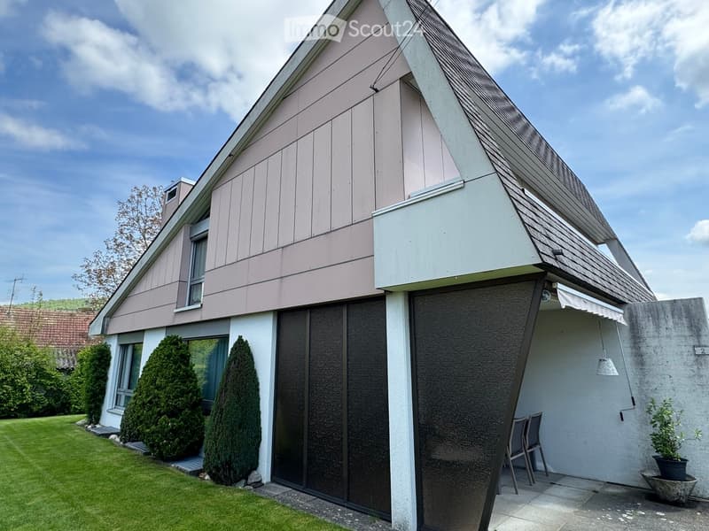 Two-story house with a modern design, featuring a garage, large windows, and a well-maintained lawn with coniferous trees.