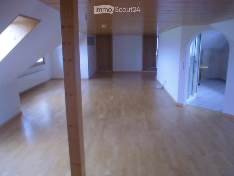 Empty hallway with wooden flooring, white walls, and a slanted ceiling. Features an open doorway leading to another room and a small window on the left side.