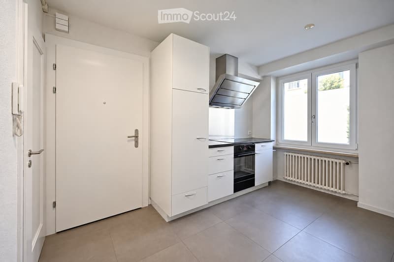 Modern kitchen with white cabinets, stainless steel range hood, oven, and radiator under windows.