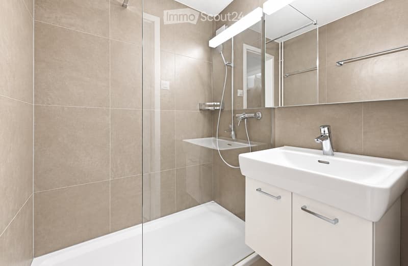 Modern bathroom with a white sink, bathtub, large mirror, and sleek chrome fixtures.