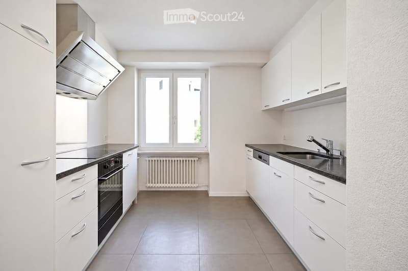 Modern kitchen with white cabinets, stainless steel appliances, and a large window. Features an oven, sink, and range hood.