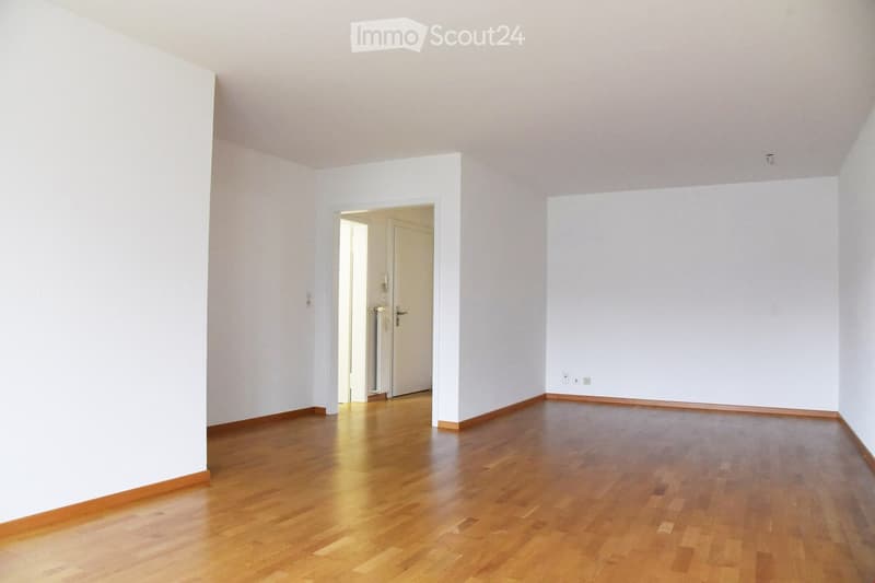 Empty room with light wooden flooring and white walls, featuring a doorway leading to another room.