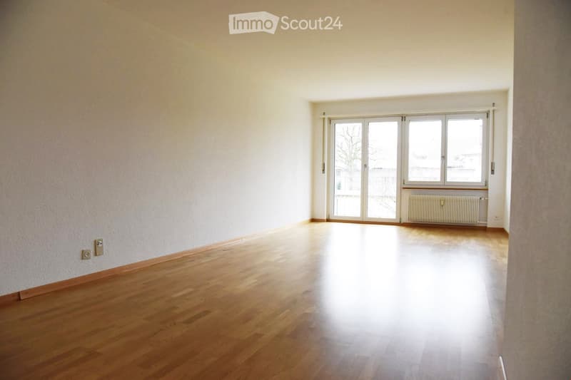 Empty room with wooden flooring, white walls, large windows, and a radiator under one window.