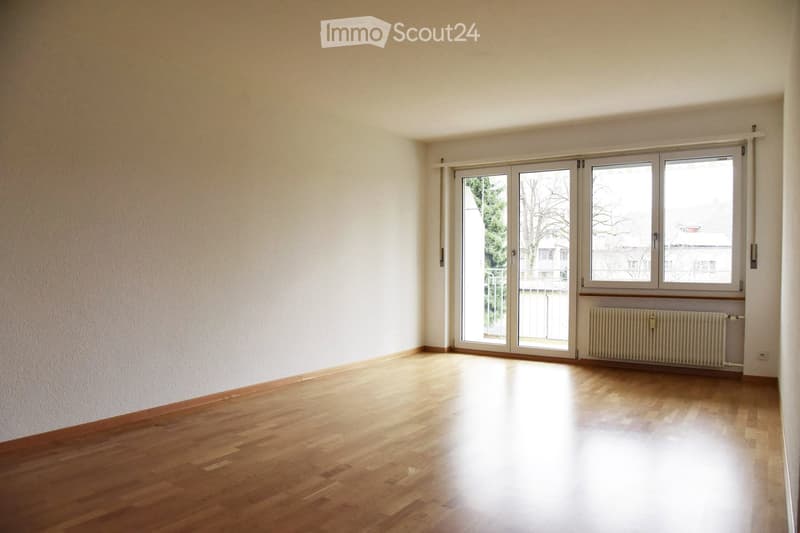 Empty room with wooden flooring, white walls, large windows, and a radiator. No furniture or personal items present.