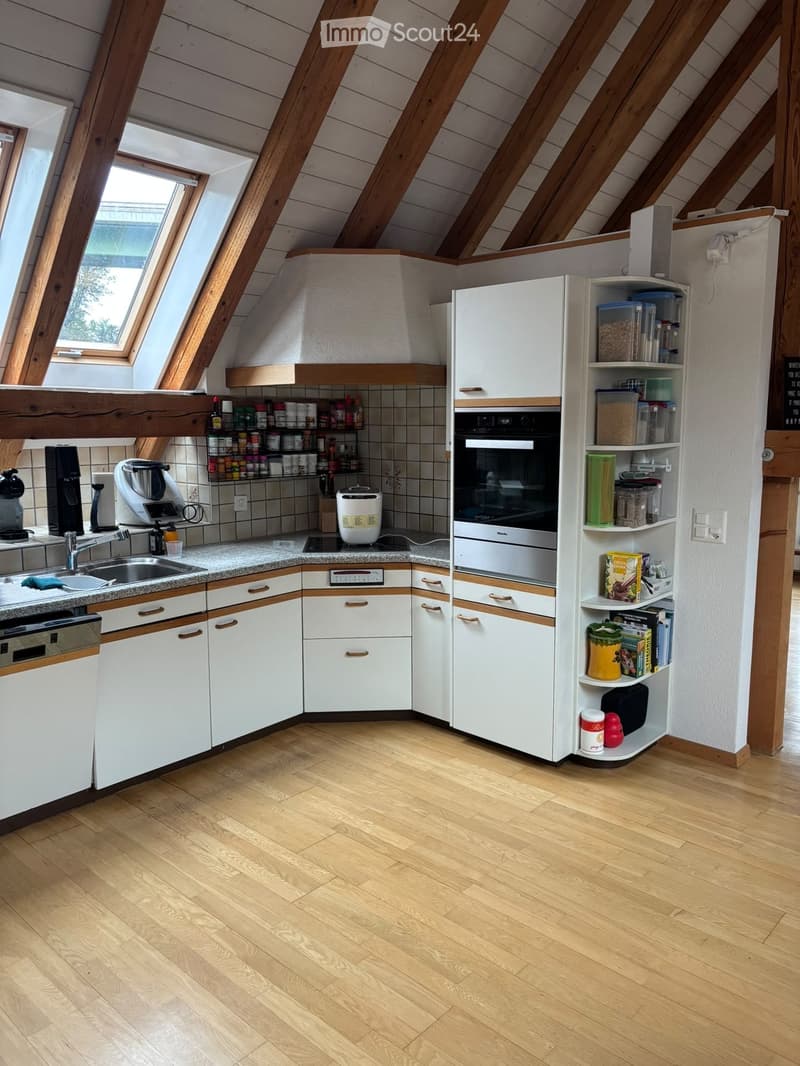 Modern kitchen with white cabinets, wooden beams, and a skylight window. Features include a sink, oven, refrigerator, microwave, coffee maker, and various kitchen items on shelves.