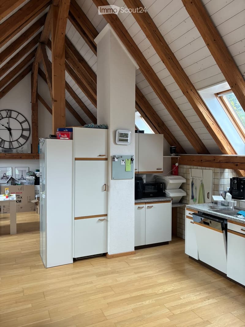 Attic kitchen with wooden beams, white cabinets, a refrigerator, microwave, sink, and a clock on the wall.
