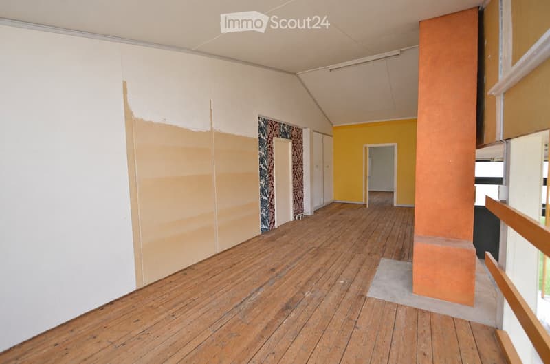 Empty room with wooden flooring, white walls, and a partially painted wall in yellow. There are doors leading to other rooms and a visible staircase railing.