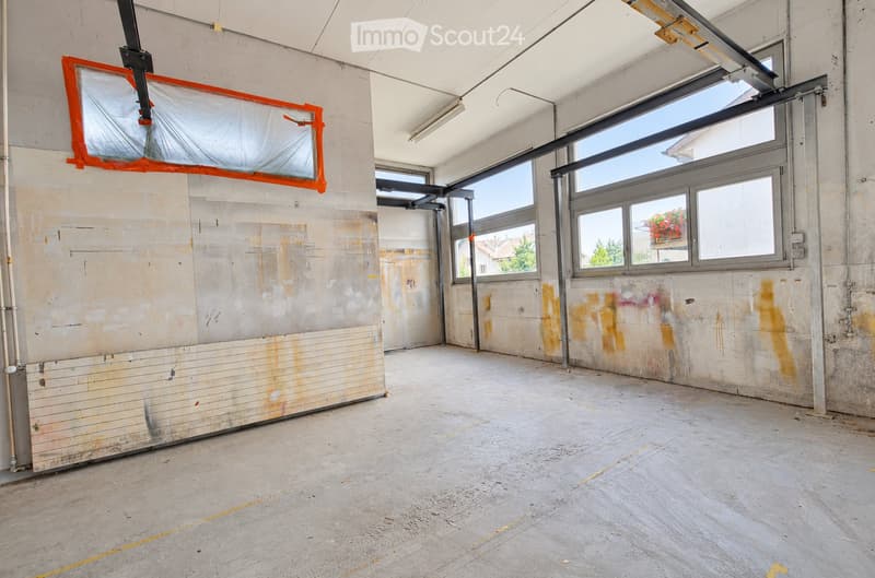 Empty room with bare concrete walls and floor, large windows, and exposed structural elements.