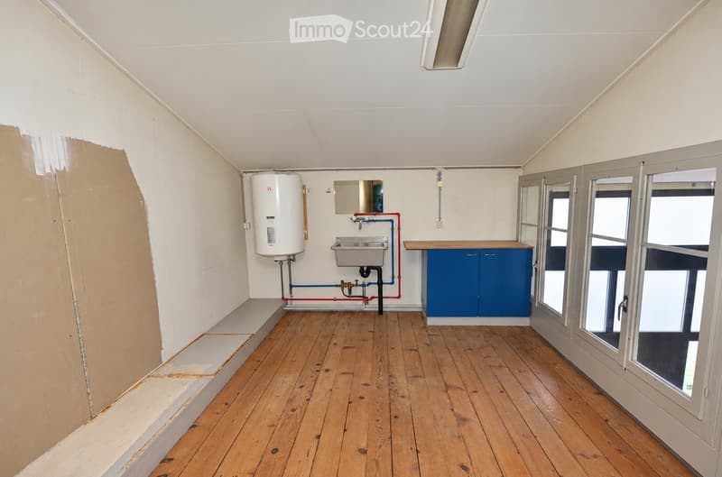 Empty room with wooden flooring, white walls, and a slanted ceiling. Features include a water heater, sink, and blue cabinets.