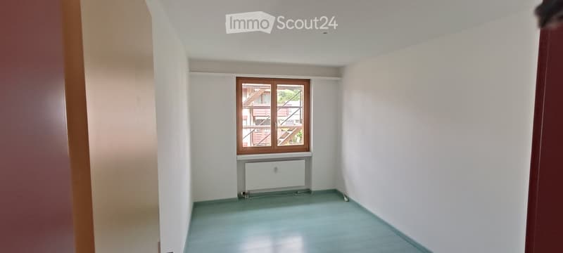 Empty room with light blue flooring, white walls, a window with wooden frame, and a radiator below the window.
