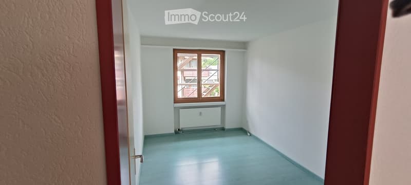 Empty room with light blue flooring, white walls, a window with wooden frame, and a radiator below it.