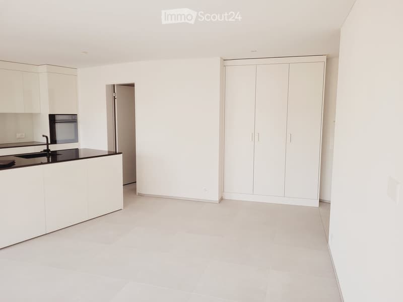 Empty kitchen with white cabinets, a black countertop, and a built-in oven. The space is clean and minimalistic with no furniture or appliances visible.