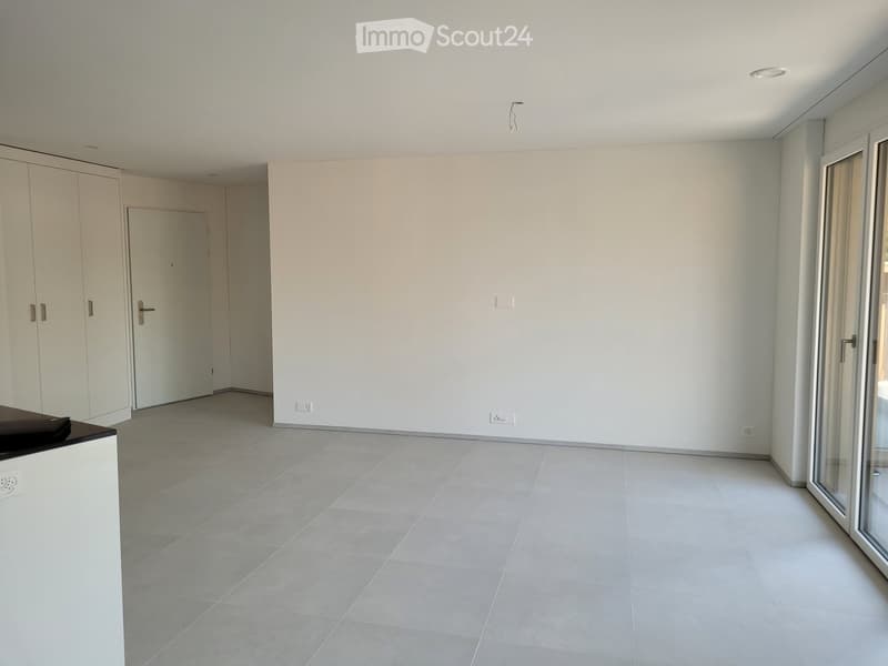 Empty room with white walls, grey tiled floor, white cabinetry, and a large glass door leading outside.
