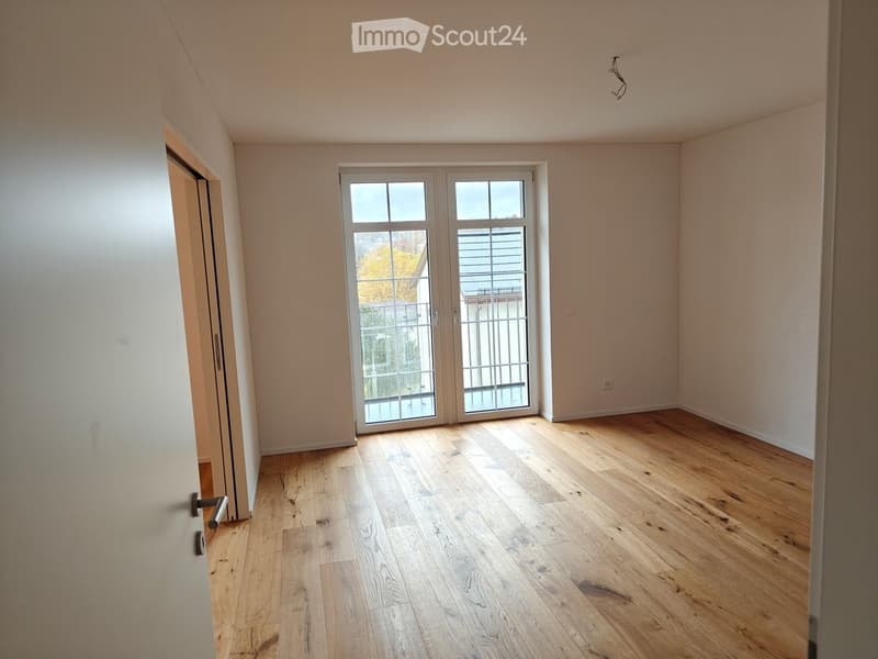 Empty room with light wooden flooring, white walls, and a large glass door leading outside.