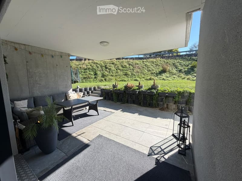 Modern outdoor patio with a concrete roof, tiled floor, sofa, coffee table, bench, lantern, and potted plants.