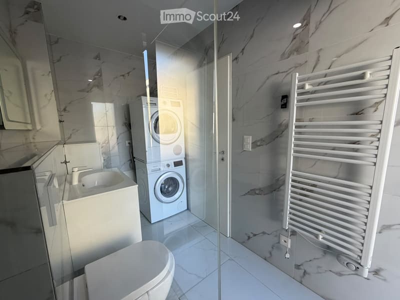 Modern bathroom with white marble tiles, a sink, toilet, washing machine, and a radiator.