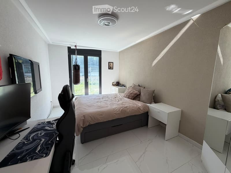 Modern bedroom with a large bed, nightstand, chair, screen, and picture frame. The room features white walls, a marble floor, and a large window with a view of the outdoors.