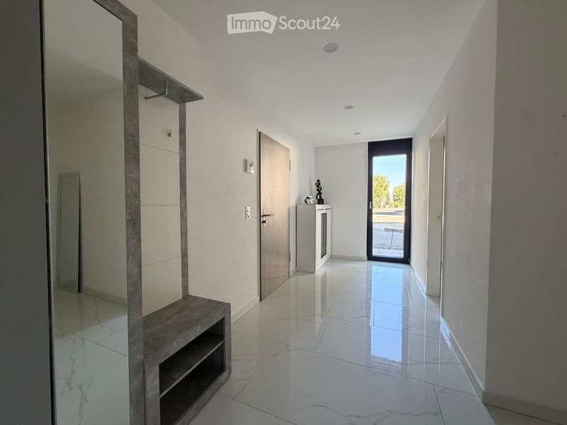 Modern hallway with white walls, polished marble flooring, recessed lighting, and a sliding glass door leading outside.