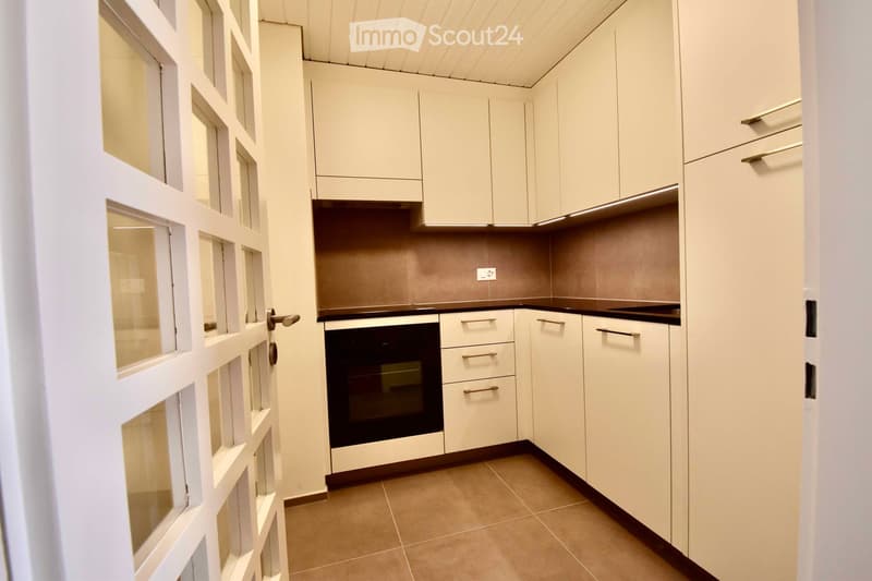 Modern kitchen with white cabinets, stainless steel oven, and tiled floor.