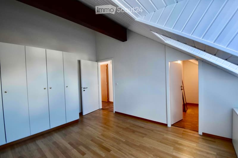 Empty room with white walls, wooden floor, built-in white closet, and two open doors leading to other rooms.