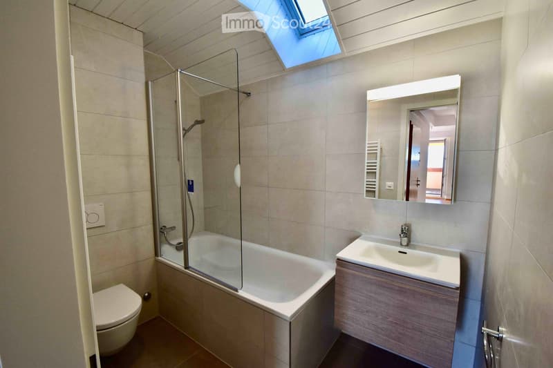 Modern bathroom with a bathtub, toilet, sink, mirror, and a glass-enclosed shower area. Features a skylight window for natural light.