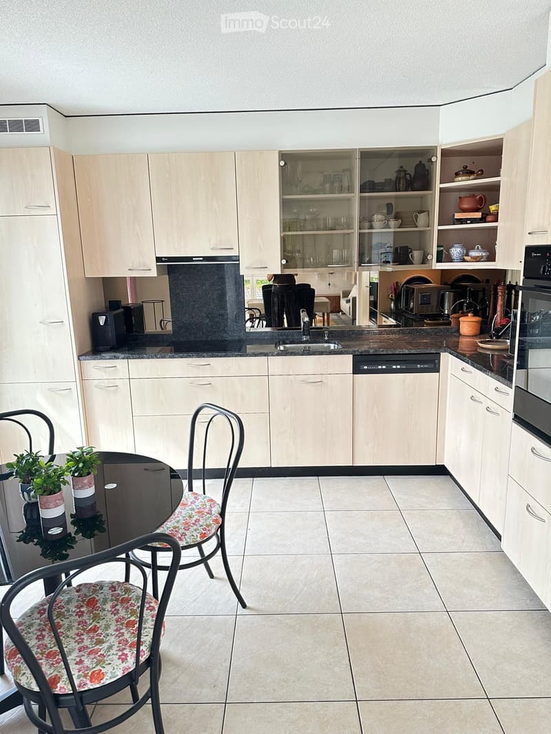 Modern kitchen with light wood cabinets, granite countertops, and stainless steel appliances. Features a dining area with a round table and two chairs.