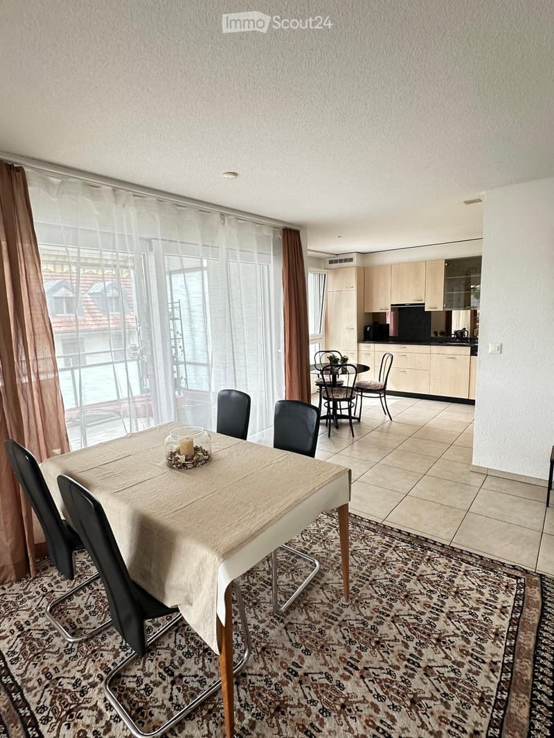 A well-lit dining area with a table, chairs, and a candle centerpiece, connected to a modern kitchen with cabinets and a counter.