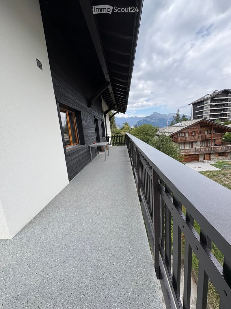 Balcony with a view of mountains, a small table, and a railing.