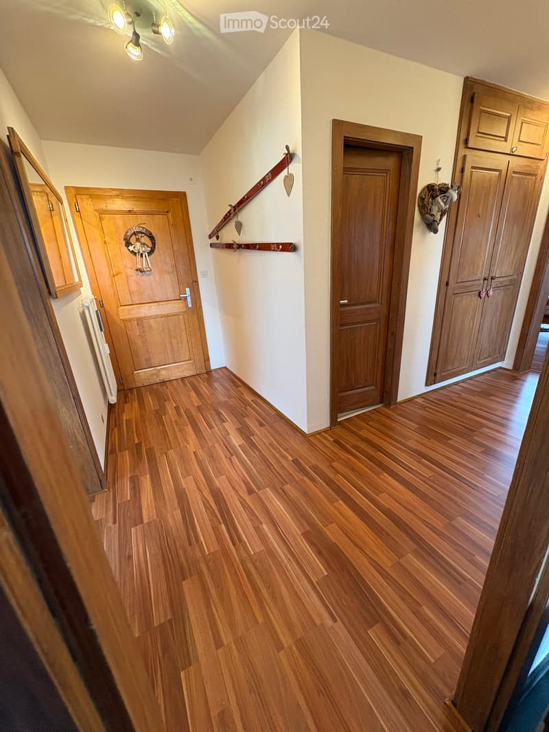 A well-lit hallway with wooden flooring, multiple wooden doors, and decorative wall-mounted skis and a heart-shaped ornament.