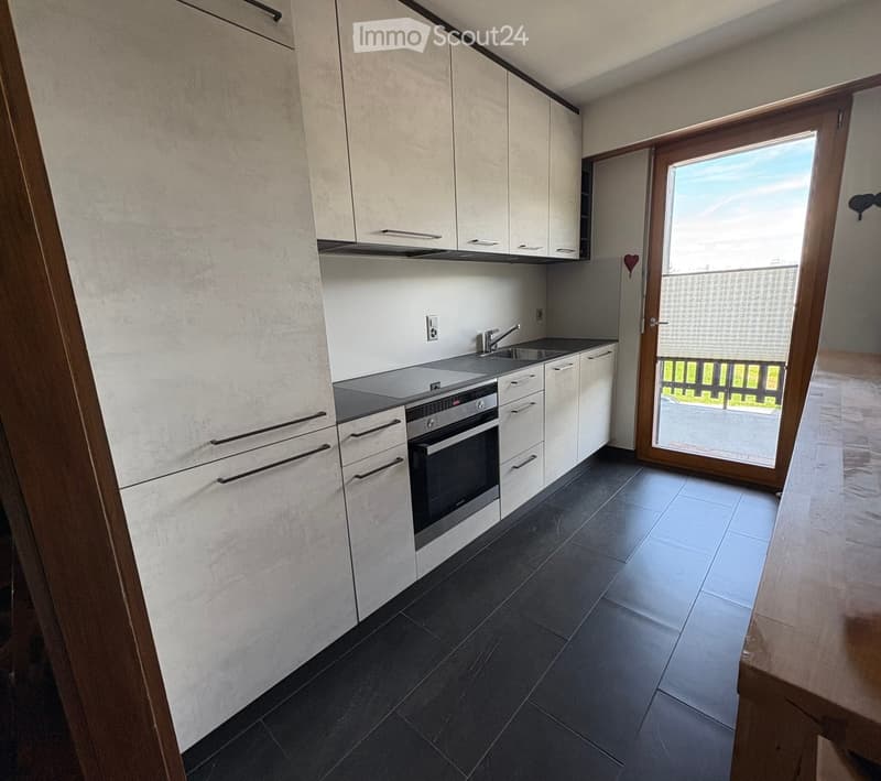 Modern kitchen with white cabinets, black tiled floor, stainless steel oven, sink, and faucet. A sliding glass door leads to a balcony.