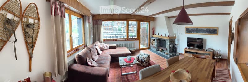 Cozy living room with wooden beams, large windows offering a scenic view, a sectional sofa, coffee table, ottoman, dining table with chairs, television, fireplace, and decorative items.