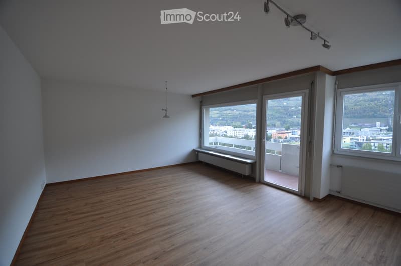 Empty room with wooden flooring, large windows, and a sliding door leading to a balcony.