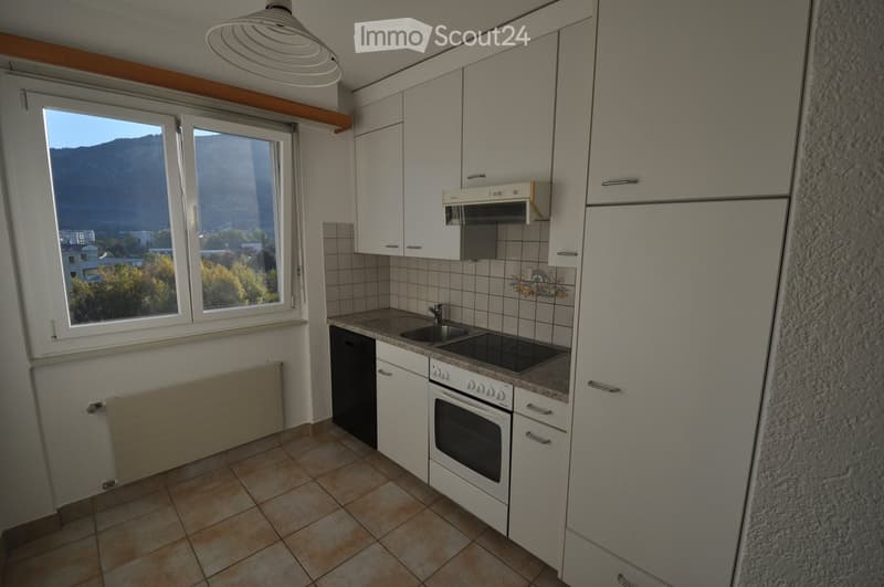 Modern kitchen with white cabinets, stainless steel appliances, and a view of mountains through large windows.