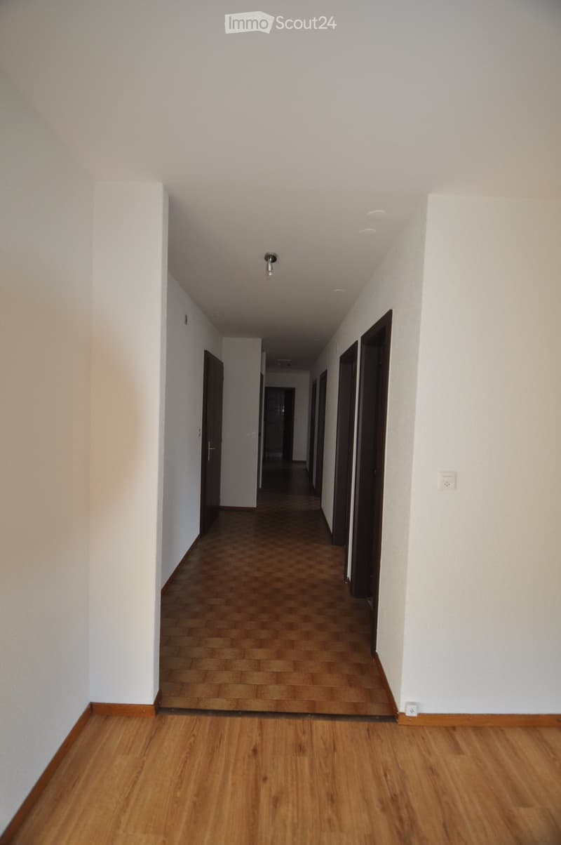Empty hallway with wooden flooring, white walls, and several closed doors along both sides.
