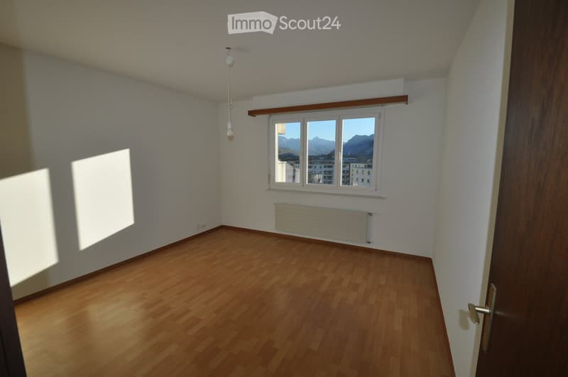 Empty room with wooden flooring, white walls, a window with a scenic mountain view, and a radiator below the window.