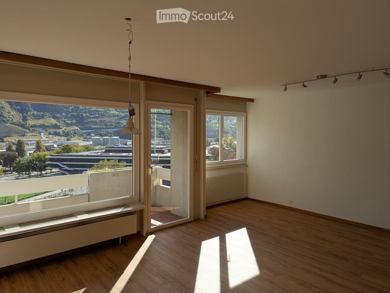 Empty room with wooden flooring, large windows, and a view of the city and surrounding landscape.
