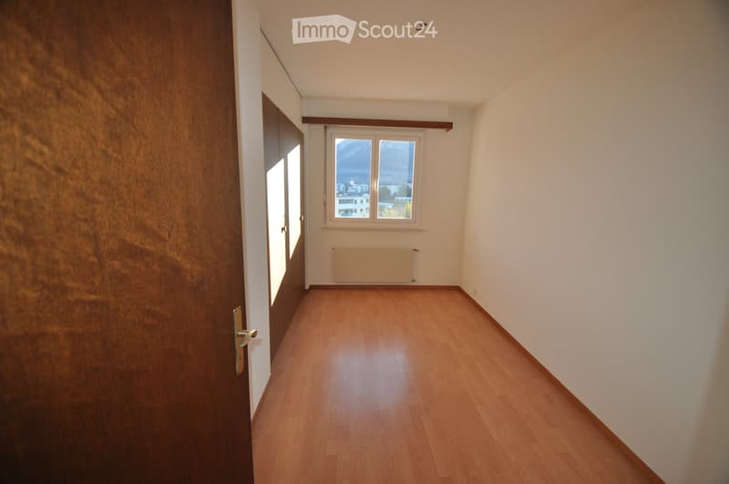 Empty room with wooden flooring, white walls, a window with a view, and a radiator. No furniture or equipment is present.